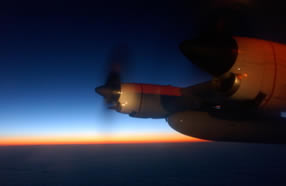 The sun rises off the right side of a Coast Guard C-130 Hercules airplane